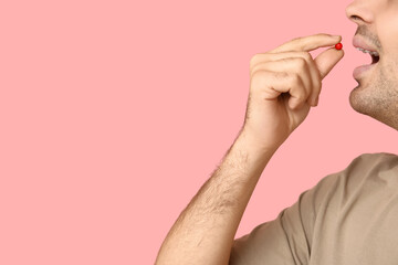 Young man taking vitamin A pill on pink background, closeup