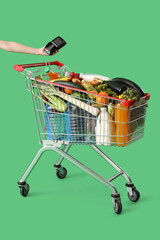 Shopping cart full of food and female hand with payment terminal on green background