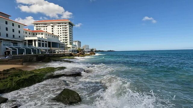 waves crashing on the shore of old san juan puerto rico with tall hotel building in the background (caribbean travel tourism destination) sj pr sea coast rocky shore beach condado
