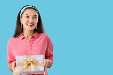 Beautiful young Asian woman with gift box on blue background