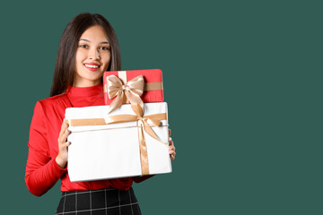 Beautiful young Asian woman with gift boxes on green background