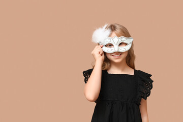 Little girl wearing carnival mask on beige background