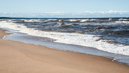 Waves Crashing on a Sandy Beach Shoreline Under a Bright Blue Summer Sky