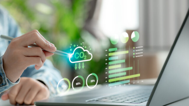 Close-up of hand using pen to interact with CO2 emissions dashboard hologram, displaying eco data, cloud icon, and environmental analytics, symbolizing carbon tracking and green technology.