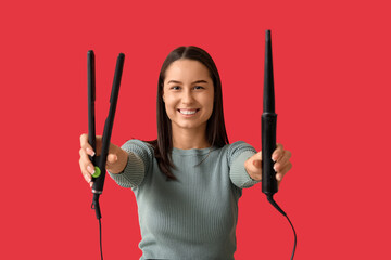Female hairdresser with curling iron and flattening iron on red background