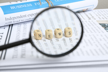 Magnifying glass, newspapers and word NEWS made of cubes, closeup