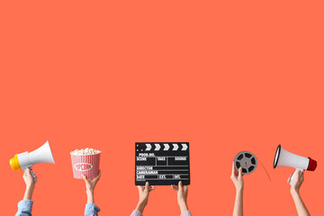 Many hands with bucket of popcorn, movie clapper and megaphones on orange background