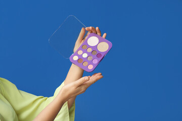 Woman's hands with palette of eyeshadows on blue background