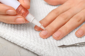 Female hands applying cuticle oil onto fingernails on white towel, closeup