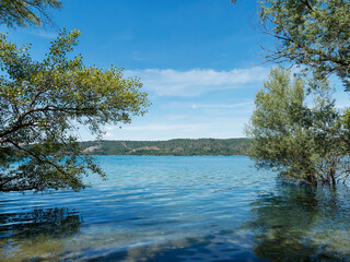  Les eaux turquoises du lac de Sainte-Croix depuis la rive sud le long du sentier GR 99 depuis Bauduen avec vue sur le pont et Barrage ainsi que les gorges de Bodinard à l'horizon 
