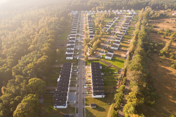 Aerial view of a modern residential development with white houses next to a forest at sunrise