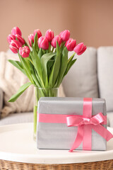 Vase with flowers and gift box on coffee table in living room