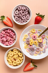 Bowls of colorful sweet cereal rings with milk and strawberries on brown background