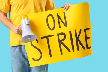 Protesting young man holding placard with text ON STRIKE and megaphone against blue background,...