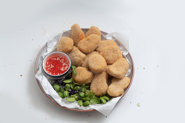 Breaded chicken nuggets with sauce and salad on a plate on a white background