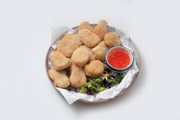 Breaded chicken nuggets with sauce and salad on a plate on a white background
