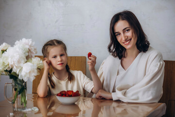 A family of mother and daughter together in the kitchen at the table eating strawberries, beautiful...