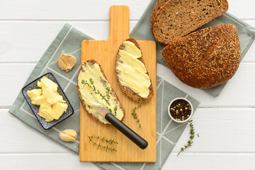 Board of bread slices with fresh butter, garlic and peppercorn on white wooden background