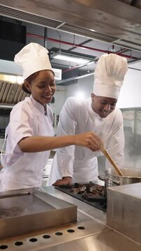 African woman chef and male chef cooking together in restaurant kitchen, showing teamwork and culinary skills.