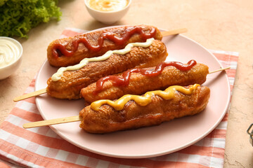 Plate of tasty corn dogs with different sauces on beige background