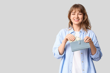 Beautiful young woman putting money in wallet on grey background
