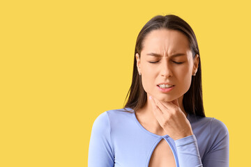 Young woman suffering from sore throat on yellow background