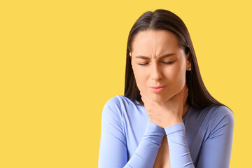 Young woman suffering from sore throat on yellow background