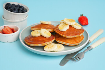 Tasty pancakes with honey and banana on blue background