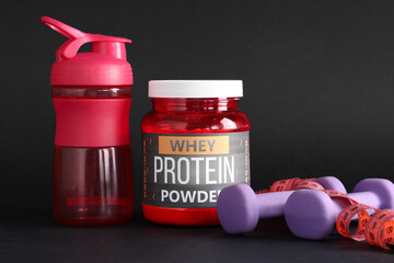 Sports water bottle, protein powder, dumbbells and measuring tape on dark background