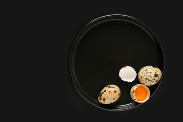 Plate with raw quail eggs on black background