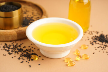 Bowl of oil with sesame seeds and fish oil capsules on beige background