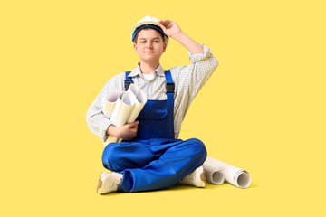 Teenage architect with house plans sitting on yellow background