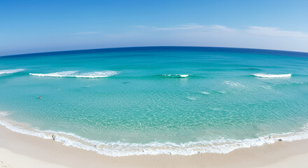 Bright turquoise ocean waves gently crashing onto white sandy beach under clear blue sky with distant horizon and calm sea surface