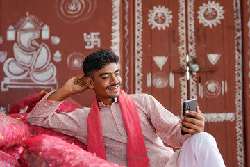 young indian farmer holding smartphone at home