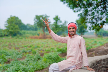 young indian farmer standing at green agricultural field