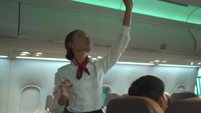 Female flight attendant closes the overhead luggage compartment before takeoff, ensuring safety and comfort for passengers