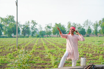 young indian farmer standing at field talking on smartphone