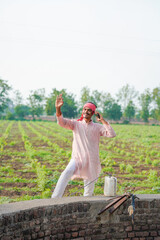 young indian farmer standing at field talking on smartphone