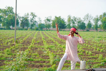 young indian farmer standing at field talking on smartphone