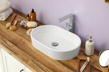 Chest of drawers with sink and bath supplies near lilac wall in bathroom