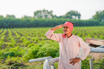 young indian farmer standing at green agricultural field