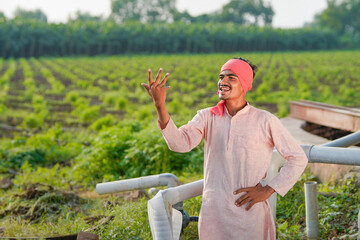 young indian farmer standing at green agricultural field