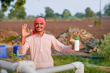 Young indian farmer showing liquid fertilizer bottle at field
