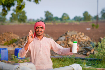 Young indian farmer showing liquid fertilizer bottle at field