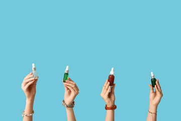 Female hands with different bottles of cosmetic products on blue background