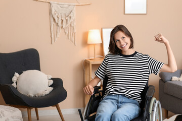 Young pretty woman in wheelchair showing strength gesture at home
