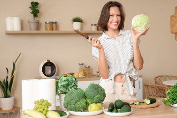 Beautiful young happy woman with different fresh green vegetables on table in kitchen