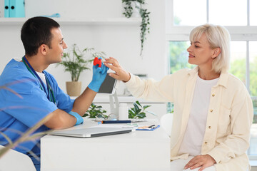 Fototapeta premium Male endocrinologist showing thyroid gland model to female patient at table in clinic