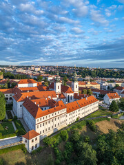 Obraz premium Strahov Monastery captures the serene beauty of Prague at sunrise, with its stunning architecture and surrounding greenery. The aerial view showcases the vibrant rooftops and peaceful atmosphere.