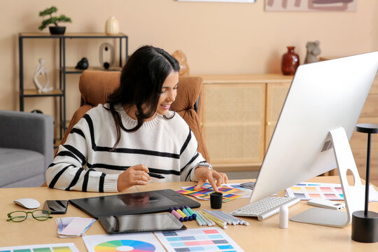 Young female graphic designer working with tablet and color palettes at table in office